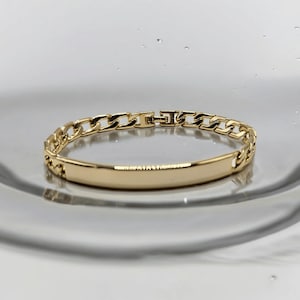 May include: A gold chain bracelet with a flat, rectangular tag. The tag is smooth and has no inscription.