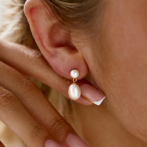 May include: A pair of gold earrings with two white pearls, one smaller pearl at the top and a larger pearlescent pearl dangling below.