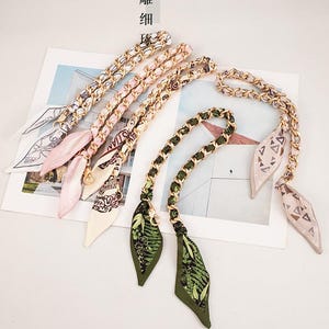 May include: A selection of handbag chain straps with decorative silk scarves. The straps have gold-coloured chain links and attached scarves in shades of pink, green, and cream, with floral and geometric patterns. Chinese text is also visible.