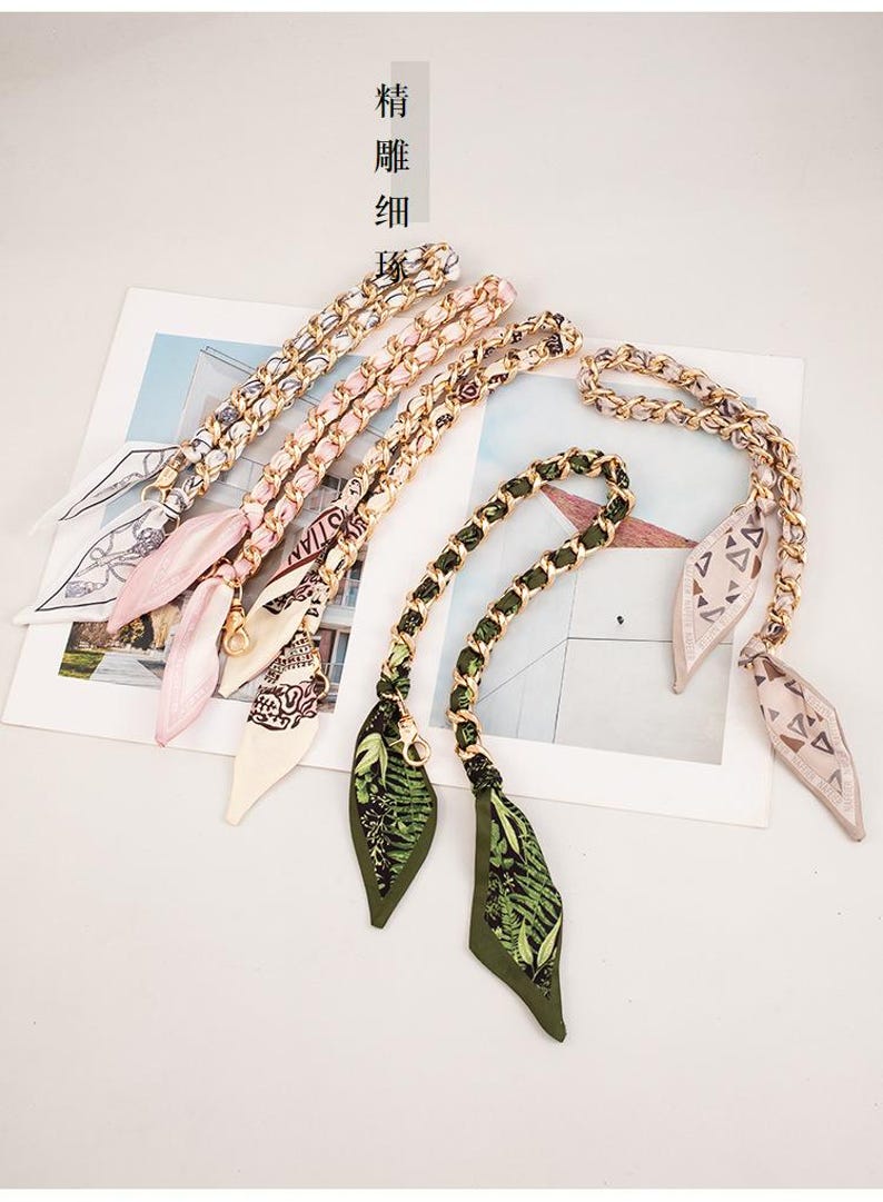 May include: A selection of handbag chain straps with decorative silk scarves. The straps have gold-coloured chain links and attached scarves in shades of pink, green, and cream, with floral and geometric patterns. Chinese text is also visible.
