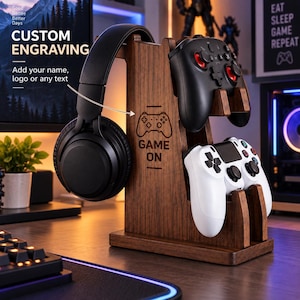 Puede incluir: Un soporte de madera marrón oscuro para juegos con un soporte vertical, un colgador de auriculares a la izquierda y dos cunas para mandos a la derecha. El soporte está grabado con un icono de mando y el texto GAME ON. Sostiene auriculares negros, un mando negro y un mando blanco.