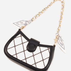 May include: A black and white handbag with a chain strap and a small scarf detail. The bag features a white surface with a brown grid pattern, black trim, and a black clasp.