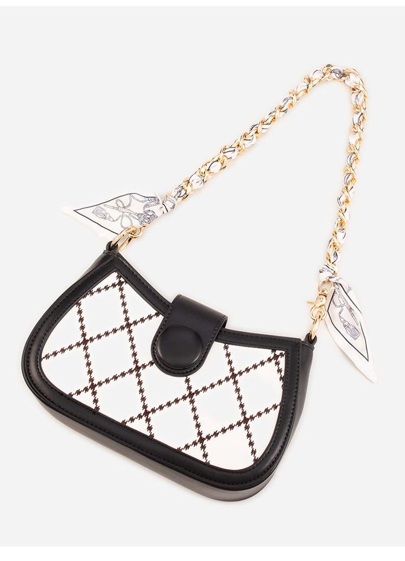 May include: A black and white handbag with a chain strap and a small scarf detail. The bag features a white surface with a brown grid pattern, black trim, and a black clasp.