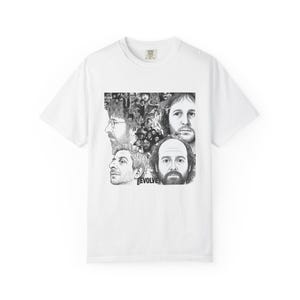May include: White t-shirt featuring a black and white graphic of several faces and the word "EVOLVE". The graphic includes portraits of men with various hairstyles and facial hair. The shirt has a crew neck and short sleeves.
