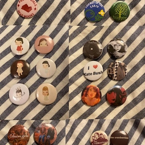 May include: A collection of circular pin-back buttons featuring various designs including text such as The book is better, Save the Earth, Tax Big Oil, I love books, Save our libraries, Pretty girls read books, Kate Bush, Gilmore girls, and The Cranberries.