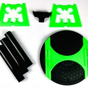 May include: A disassembled black and green table. The table components include a black circular tabletop with a green accent, three black cylindrical legs, two green plastic supports, and a small black plastic connector.