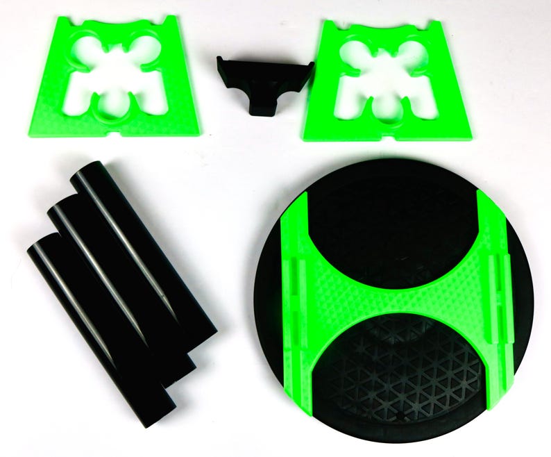 May include: A disassembled black and green table. The table components include a black circular tabletop with a green accent, three black cylindrical legs, two green plastic supports, and a small black plastic connector.