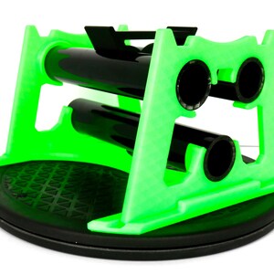 May include: A bright green wine bottle holder with a black base and black bottle supports. The holder is designed to cradle two bottles, with a circular opening for each bottle. The base is round and textured.