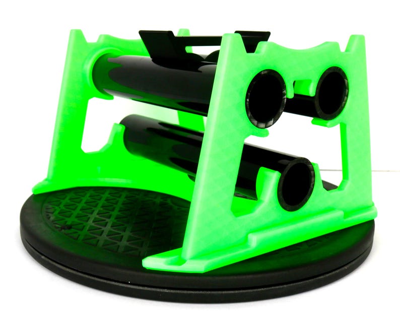 May include: A bright green wine bottle holder with a black base and black bottle supports. The holder is designed to cradle two bottles, with a circular opening for each bottle. The base is round and textured.