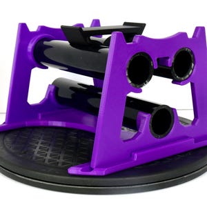 May include: A purple and black wine bottle holder. The holder is made of purple plastic and has a black base. It is designed to hold two wine bottles. The holder is on a black, textured surface.