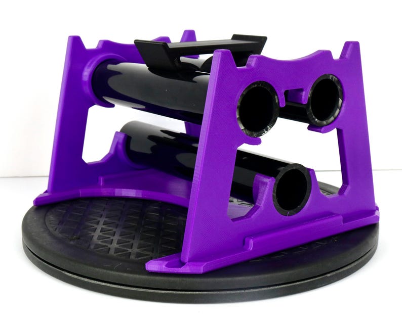 May include: A purple and black wine bottle holder. The holder is made of purple plastic and has a black base. It is designed to hold two wine bottles. The holder is on a black, textured surface.