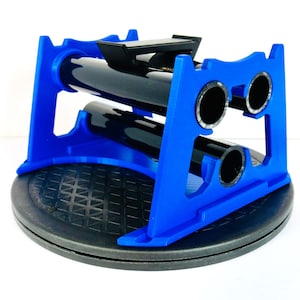 May include: A blue wine bottle holder with a black base. The holder is designed to hold two bottles horizontally. The holder is made of plastic and has a modern design. The holder is on a black, circular base.