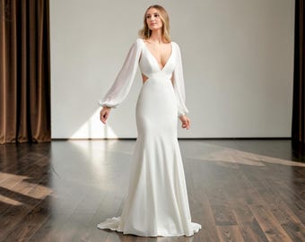May include: A white wedding gown with a plunging neckline and long, sheer sleeves. The dress features a fitted bodice, cut-out details at the waist, and a flowing mermaid skirt. The gown is made of a smooth, elegant fabric.