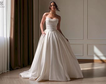 May include: A strapless ivory wedding dress featuring a fitted bodice with horizontal ruching and a sweetheart neckline. The gown has a full, floor-length skirt with a smooth satin finish and a subtle train, creating a classic and elegant silhouette.