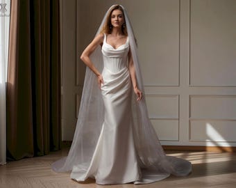 May include: A floor-length white satin wedding dress featuring a structured corset-style bodice with a scoop neckline and a draped skirt. The gown is paired with a long, sheer, floor-sweeping veil that extends beyond the hem of the dress.