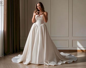 May include: A floor-length ivory satin gown featuring a structured corset-style bodice with a sweetheart neckline and a voluminous, pleated skirt that extends into a train. The garment has a smooth, lustrous finish and a fitted waistline.