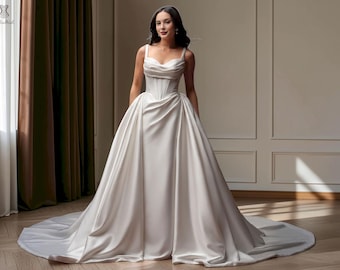 May include: A floor-length ivory satin gown featuring a structured corset-style bodice with a draped cowl neckline, thick shoulder straps, and a voluminous, pleated full skirt that extends into a circular train on the floor.