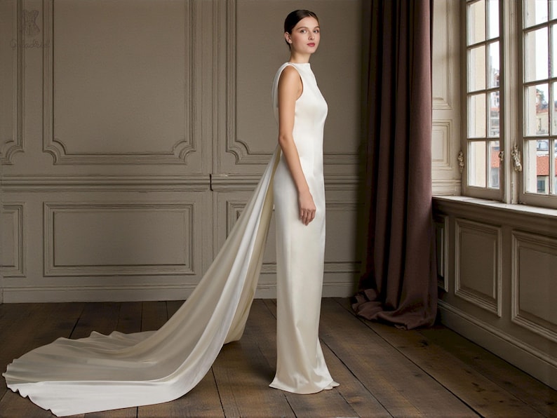 K&ouml;nnte beinhalten: Ein &auml;rmelloses, bodenlanges elfenbeinfarbenes Kleid mit langer Schleppe. Das Kleid hat einen hohen Ausschnitt und eine figurbetonte Silhouette. Die Schleppe erstreckt sich vom R&uuml;cken des Kleides und erzeugt einen dramatischen Effekt.