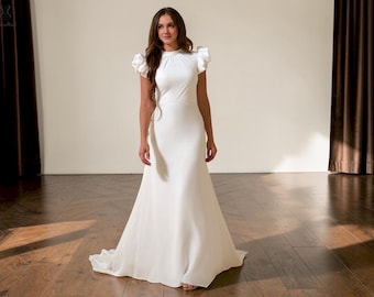 May include: A white bridal gown with a high neckline and short, ruffled sleeves. The dress has a fitted bodice and a flowing skirt that flares out from the waist. The gown is floor-length and made of a smooth, elegant fabric.