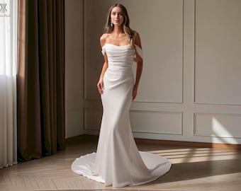 May include: A floor-length white gown featuring an off-the-shoulder neckline with draped fabric across the bodice. The dress has a fitted silhouette that flares slightly toward the hem, creating a long train that extends across the floor.