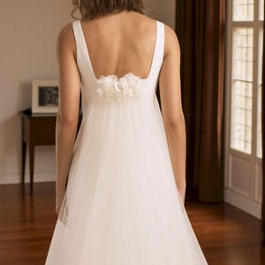 Puede incluir: Vestido de novia blanco con escote cuadrado y falda de tul fluida. La espalda presenta un adorno floral decorativo. El vestido es sencillo y elegante, adecuado para una boda o una ocasi&oacute;n especial.
