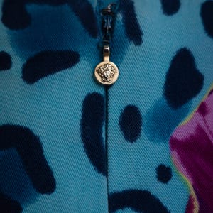 K&ouml;nnte beinhalten: Nahaufnahme eines Stoffes mit blauem und schwarzem Muster und einem goldenen Rei&szlig;verschluss-Zipper mit einem Kopf mit Krone. Der Rei&szlig;verschluss-Zipper ist rund.