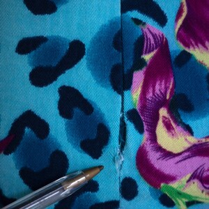 K&ouml;nnte beinhalten: Nahaufnahme eines blauen Stoffes mit einem bunten abstrakten Druck. Der Stoff hat eine Naht in der Mitte und einen kleinen Riss am unteren Rand.