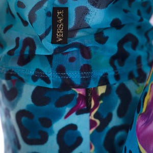 K&ouml;nnte beinhalten: Blauer Netzstoff mit einem schwarz-wei&szlig;en Leopardenmuster und dem Schriftzug "VERSACE" in goldenen Buchstaben.