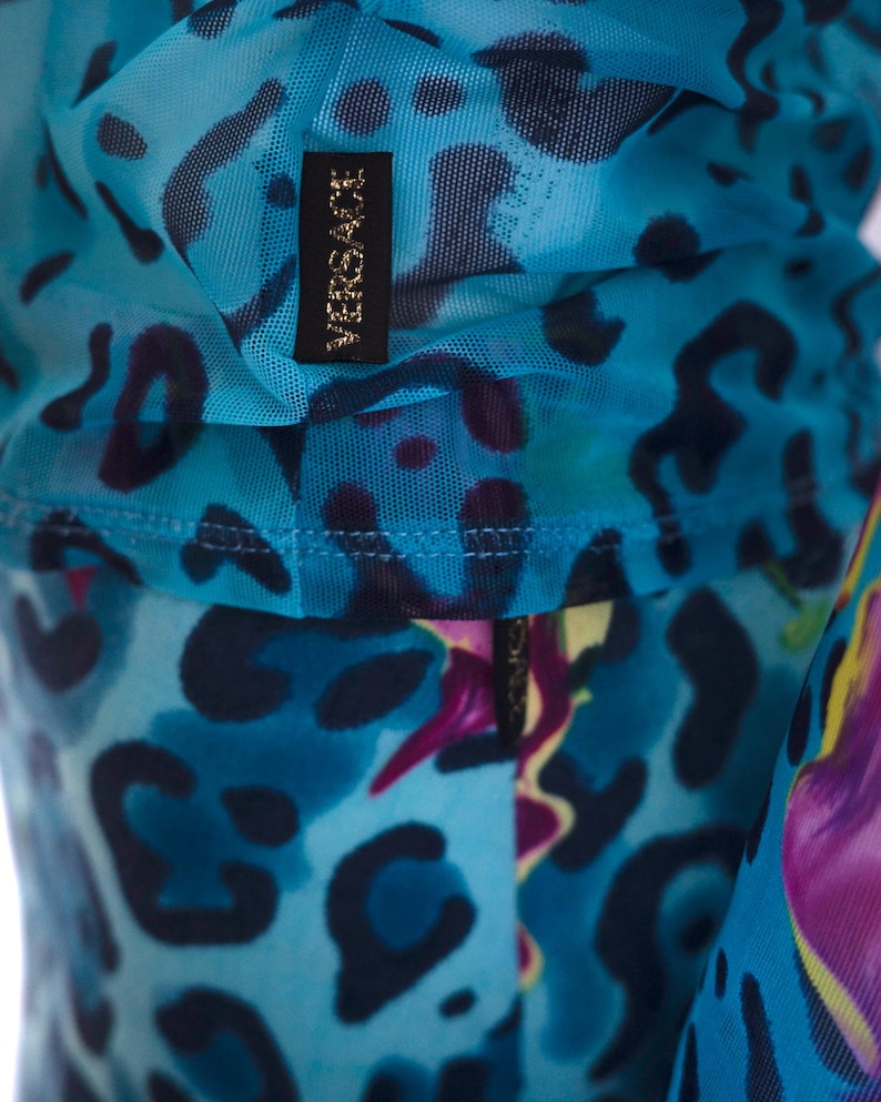 K&ouml;nnte beinhalten: Blauer Netzstoff mit einem schwarz-wei&szlig;en Leopardenmuster und dem Schriftzug "VERSACE" in goldenen Buchstaben.