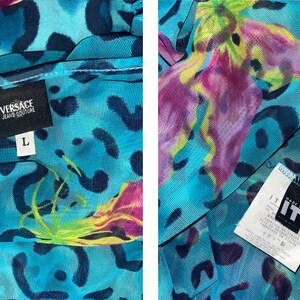 K&ouml;nnte beinhalten: Ein blaues Mesh-Oberteil mit Leopardenmuster und Blumendesign. Das Oberteil hat ein Etikett mit der Aufschrift "Versace Jeans Couture" und "L" f&uuml;r die Gr&ouml;&szlig;e.