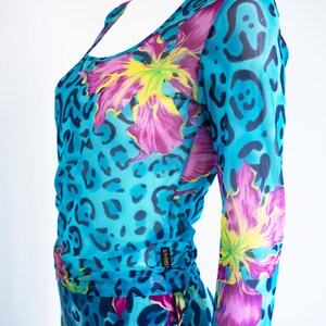 K&ouml;nnte beinhalten: Ein blaues Netz-Oberteil mit Blumen- und Leopardenmuster. Das Oberteil hat lange &Auml;rmel und einen runden Ausschnitt. Das Label "VERSACE" ist an der Seite sichtbar.