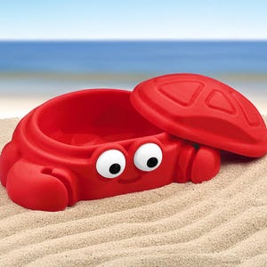 May include: Red plastic sand box shaped like a crab with a lid. The crab has googly eyes and a smiling mouth.