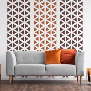 May include: A gray sofa with two orange throw pillows in front of a white wall with a geometric pattern of brown and orange triangles.