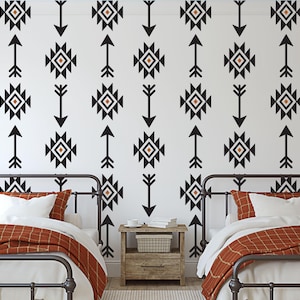 May include: Two twin beds with black metal frames and orange and white patterned bedding. The wall behind the beds is white with a black and white geometric pattern of arrows and squares.