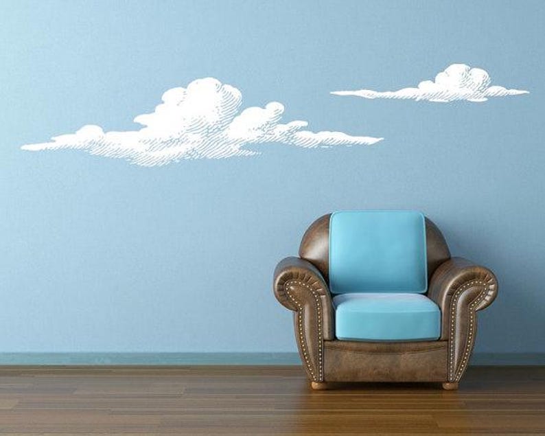 Set of 2 puffy cloud wall decals shown in white on a light blue wall next to a modern chair.