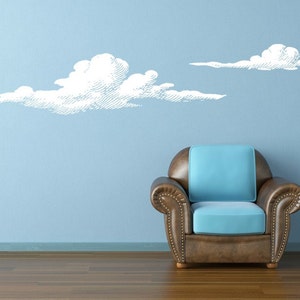 Set of 2 puffy cloud wall decals shown in white on a light blue wall next to a modern chair.