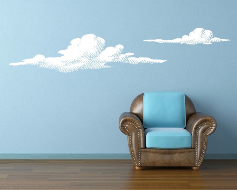 Set of 2 puffy cloud wall decals shown in white on a light blue wall next to a modern chair.