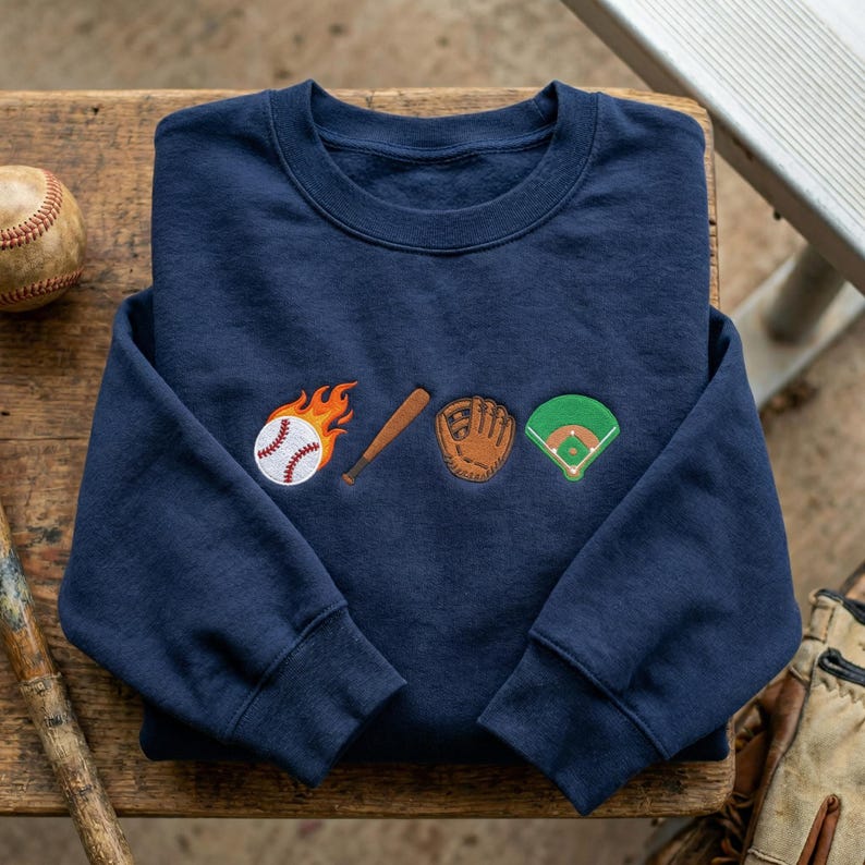 May include: Navy blue sweatshirt with embroidered baseball-themed designs. Features a baseball on fire, a wooden bat, a baseball glove, and a baseball field. The sweatshirt is made of a soft material.