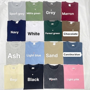 May include: An assortment of folded t-shirts in shades such as sport grey, navy, white, ash, light blue, sand, begi, black, wash, and light pink. Each shirt is labelled with its colour name.