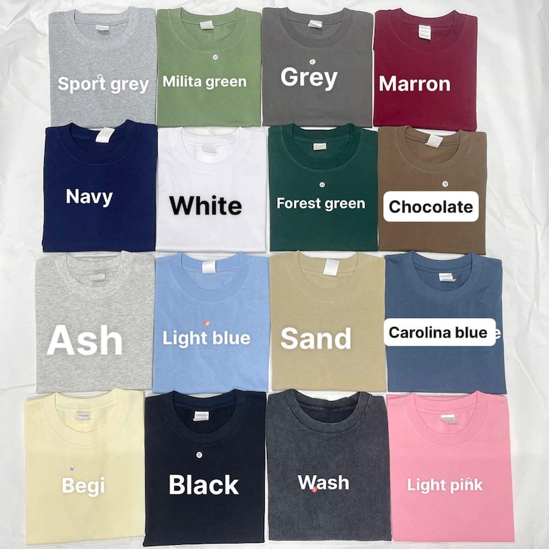 May include: An assortment of folded t-shirts in shades such as sport grey, navy, white, ash, light blue, sand, begi, black, wash, and light pink. Each shirt is labelled with its colour name.