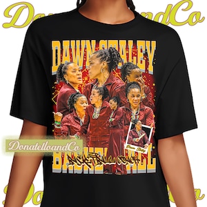 May include: Black t-shirt featuring a collage of images of Dawn Staley, with the text "DAWN STALEY BASKETBALL COACH" in gold and white. The shirt has a design with a red and gold color scheme, and the brand name "DonatelloandCo" is printed on the shirt.