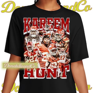 May include: Black t-shirt with a graphic print of football players in red and white uniforms. The text "Kareem Hunt" is printed in red letters on the shirt.