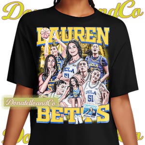 May include: Black t-shirt with a graphic print of a basketball team. The text "Lauren Betts" is printed in large letters across the top of the shirt. The team members are wearing blue and yellow uniforms with the word "UCLA" printed on them.