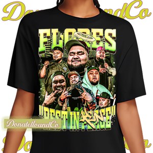May include: Black t-shirt featuring a graphic of a group of men with the word "FLORES" in yellow and green. The shirt also has the words "DESTINED IN FAITH" in yellow and green. The shirt is from DonatelloandCo.