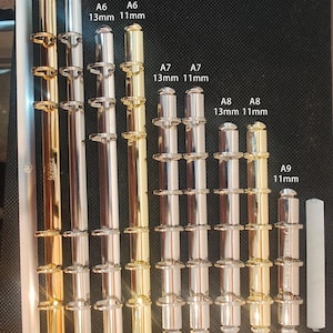 May include: An assortment of binder rings in gold, silver, and white. The image displays several sets of rings, with text indicating sizes like A6, A7, and A8, and measurements in millimeters. The text "Krause" is also visible.