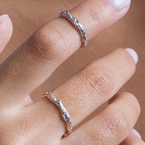 Może przedstawiać: Dwa srebrne pierścionki o fakturowanym, organicznym wzorze. Pierścionki noszone są na palcach dłoni.