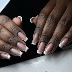 Peut inclure: Gros plan sur des mains avec des ongles longs et carrés peints d'un vernis rose clair et d'une pointe blanche en french.