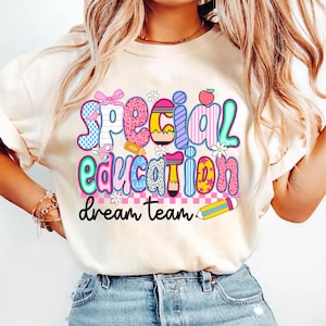 May include: Cream-coloured t-shirt featuring the text "Special Education dream team" in vibrant, playful lettering. The design incorporates a bow, scissors, flowers, an apple, and a pencil, creating a cheerful, educational theme.