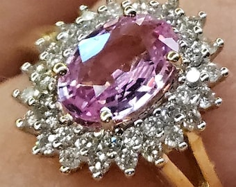 May include: A pink oval gemstone ring with a halo of smaller diamonds set in gold.
