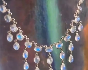 Puede incluir: Un collar de plata con un colgante de piedra lunar en forma de lágrima. El collar tiene una cadena delicada y múltiples gotas de piedra lunar.